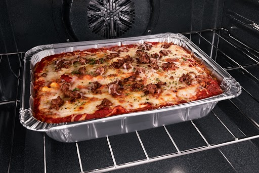 Un plat de pâtes gratinées avec des morceaux de viande sur le dessus. Le plat est aluminum se trouve sur la grille d’un four Whirlpool.