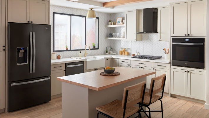 A kitchen with a Whirlpool Cooktop and Whirlpool Black Stainless Steel Double Wall Oven. On the counters are a kitchen utensil holder, bottle of oil and cutting board