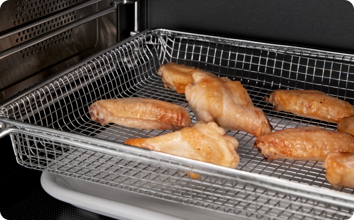 Inside a Whirlpool Oven, chicken wings cook in an air fry basket