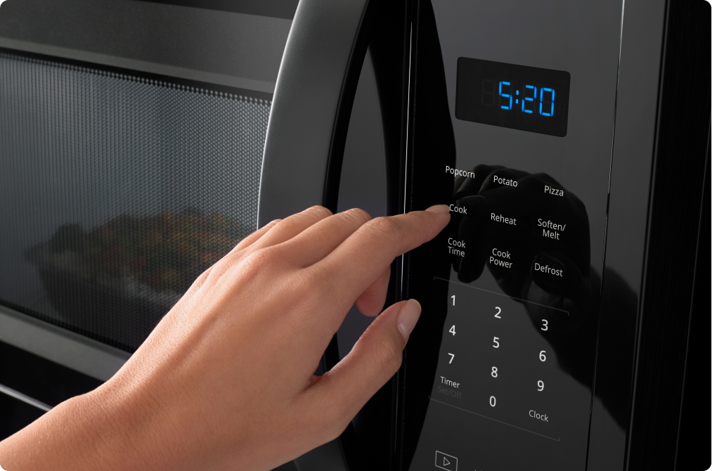 Une personne appuie sur le bouton d'un four à micro-ondes Whirlpool. L'heure indique 5:20