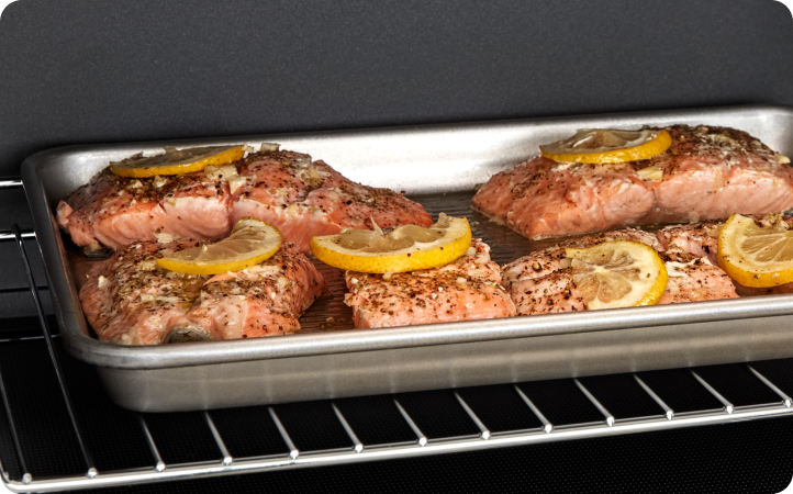 Inside a Whirlpool Oven, a baking sheet with Salmon filets topped with lemon slices cooks