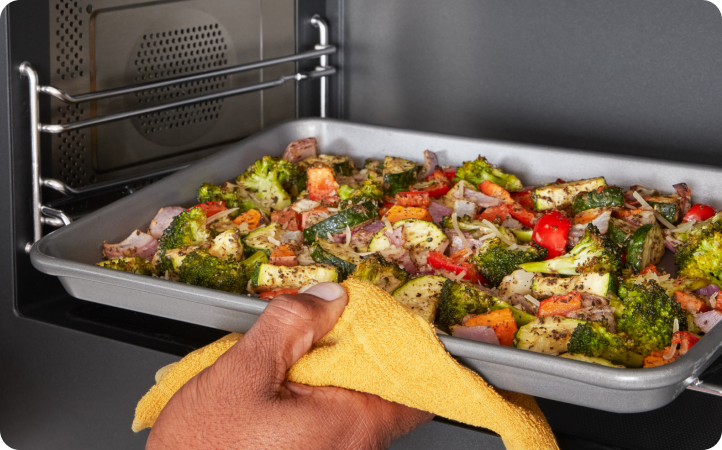 Une personne sort une plaque de cuisson de légumes d'un four Whirlpool