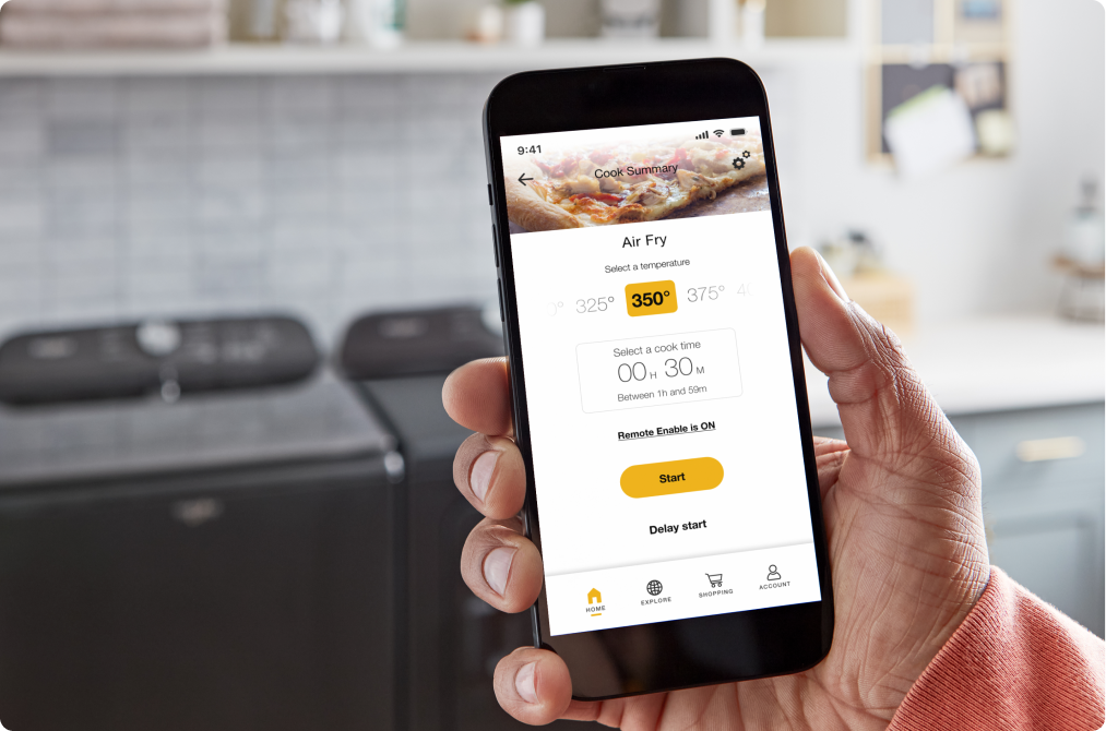 Someone holds a smartphone with the Whirlpool app on its screen. The app shows the cooking setting (air fry) and the time remaining (30 seconds)