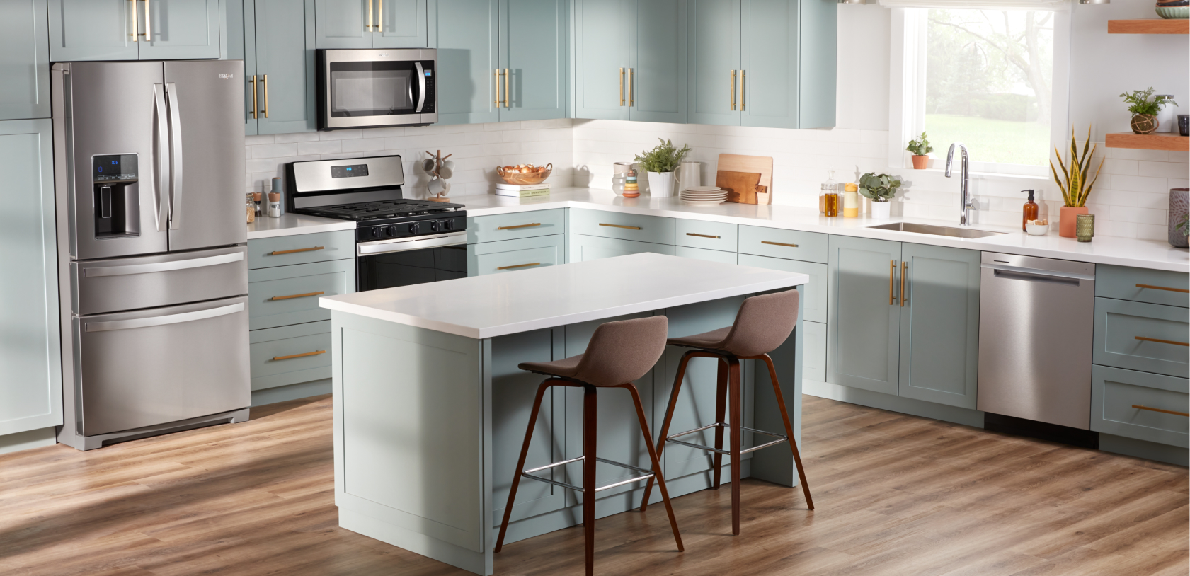 A kitchen with a Whirlpool French Door Refrigerator, a Whirlpool Oven with an Over-the-Range Microwave and a Whirlpool Dishwasher. There's an island with two chairs and on the counters are potted plants, cutting boards, mugs hanging on a stand and other items