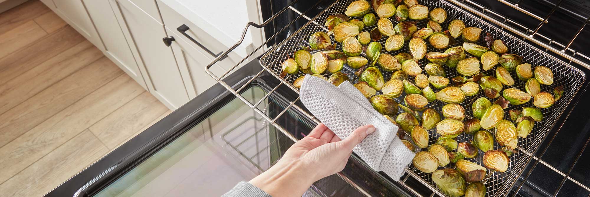 Une personne sort un panier à friture rempli de choux de Bruxelles rôtis d'un four Whirlpool à l'aide d'un chiffon à vaisselle
