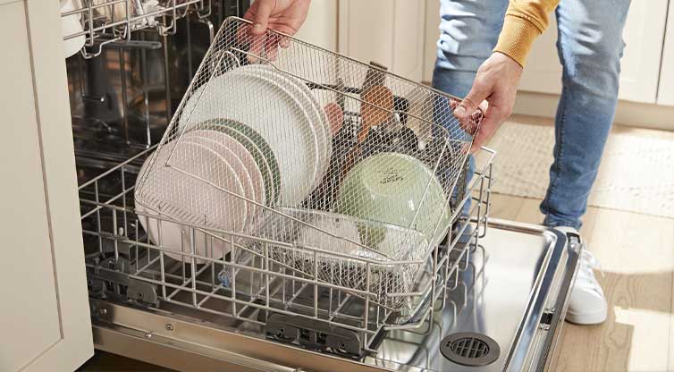 Une personne vide un panier à friture à air de son lave-vaisselle Whirlpool, dont le panier inférieur est sorti. Le panier inférieur contient également des assiettes, des bols et un panier à ustensiles