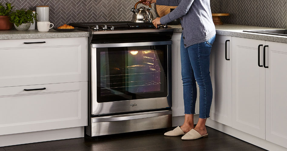 Une femme place une bouilloire sur une cuisinière au gaz en acier inoxydable Whirlpool.
