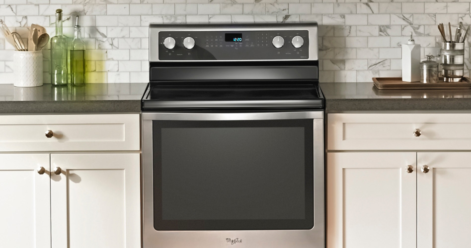 Une cuisinière en acier inoxydable Whirlpool avec une surface de cuisson en vitrocéramique dans une cuisine avec des comptoirs blancs.