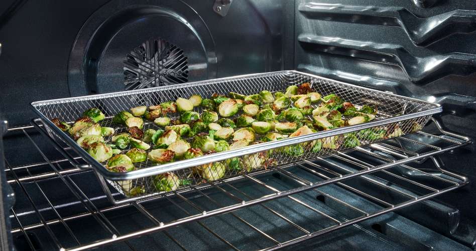 Inside an oven, Brussels sprouts cook in an air fry basket.