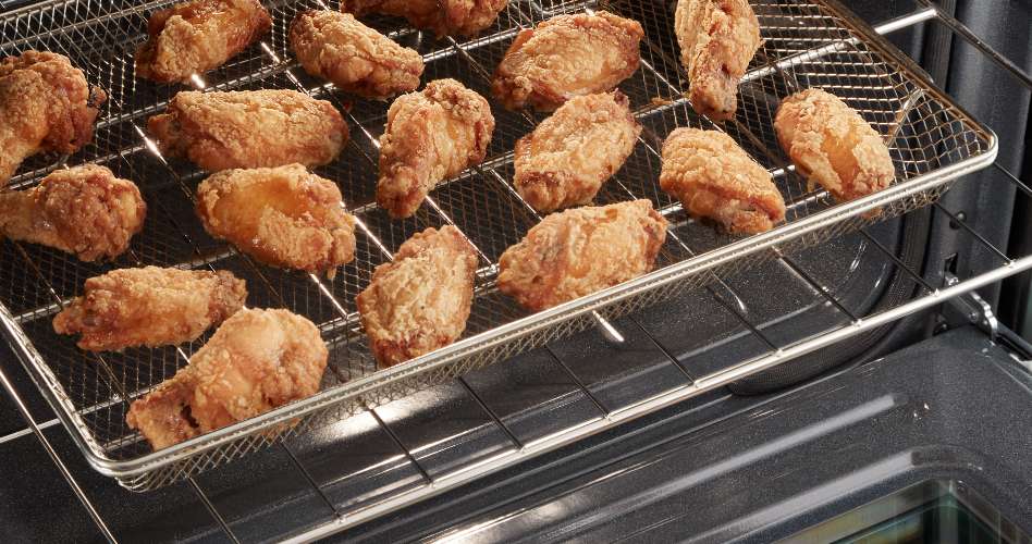 On a pulled out oven rack, chicken wings cook in an air fry basket.