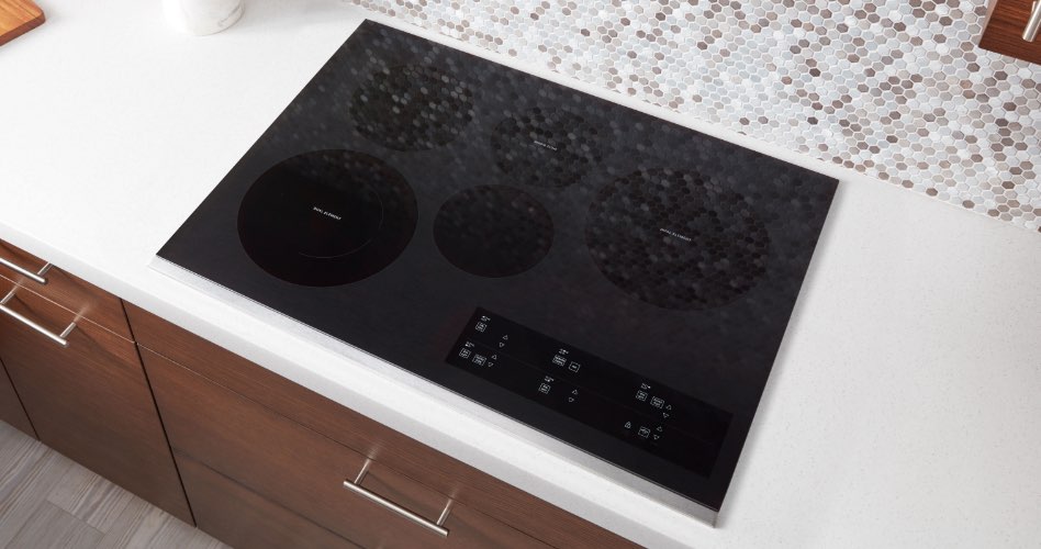 Une table de cuisson à induction Whirlpool. Sur le comptoir, il y a un bol avec des pommes et une bouteille d'huile.