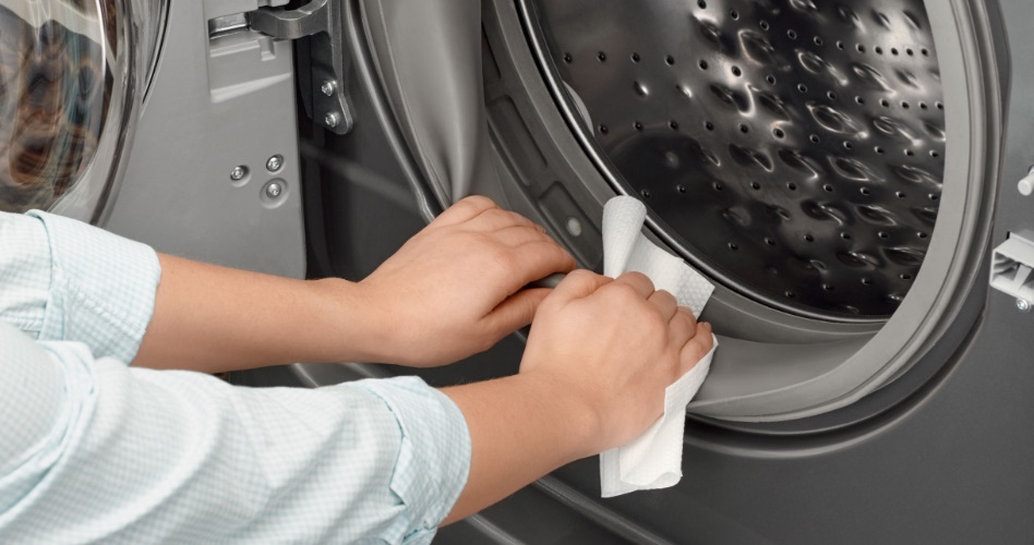 Une personne nettoie l'intérieur d'une porte de laveuse à chargement frontal avec un chiffon blanc