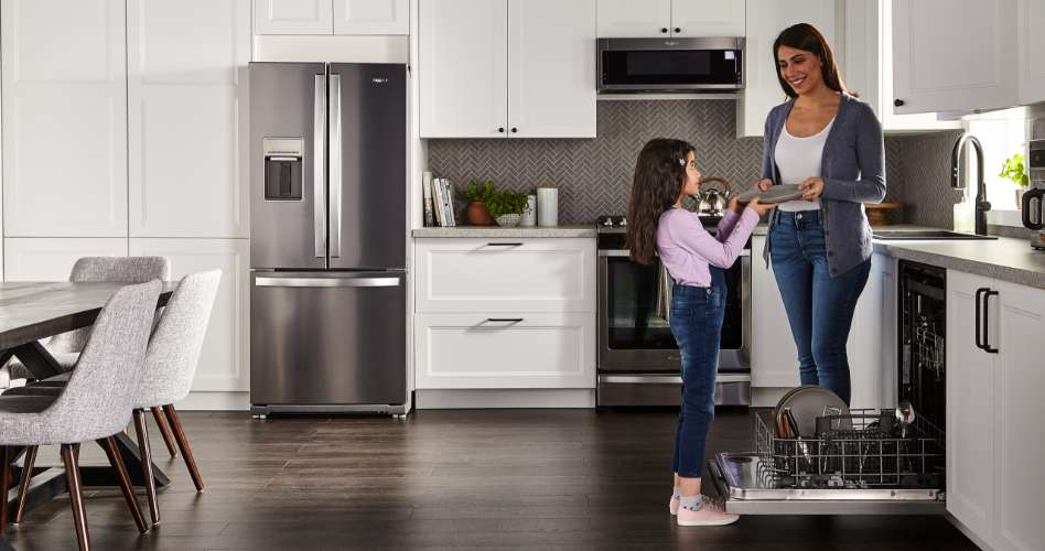 Whirlpool Combination Microwave Une mère tend une assiette à son enfant dans une cuisine. Un lave-vaisselle Whirlpool est ouvert et le panier inférieur est sorti. Sur le panier se trouvent une assiette, des couverts et des ustensiles. Dans la cuisine, on trouve un réfrigérateur Whirlpool, un four Whirlpool avec un four à micro-ondes Whirlpool, un évier, une table avec trois chaises et divers objets sur le comptoir
