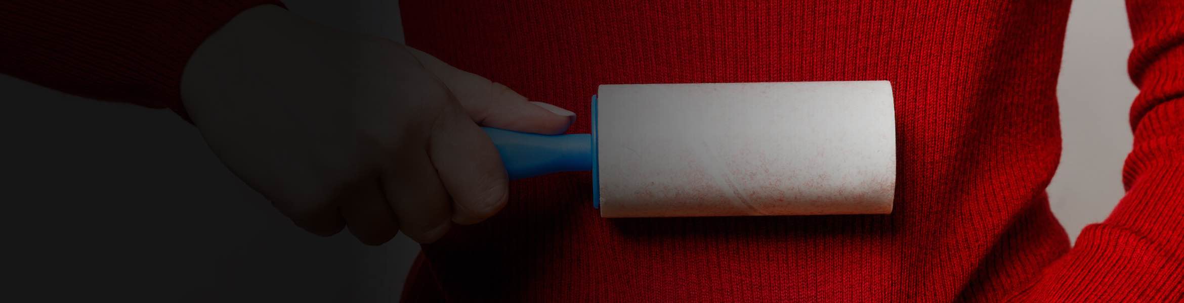 A person holds a lint roller up against a red sweater