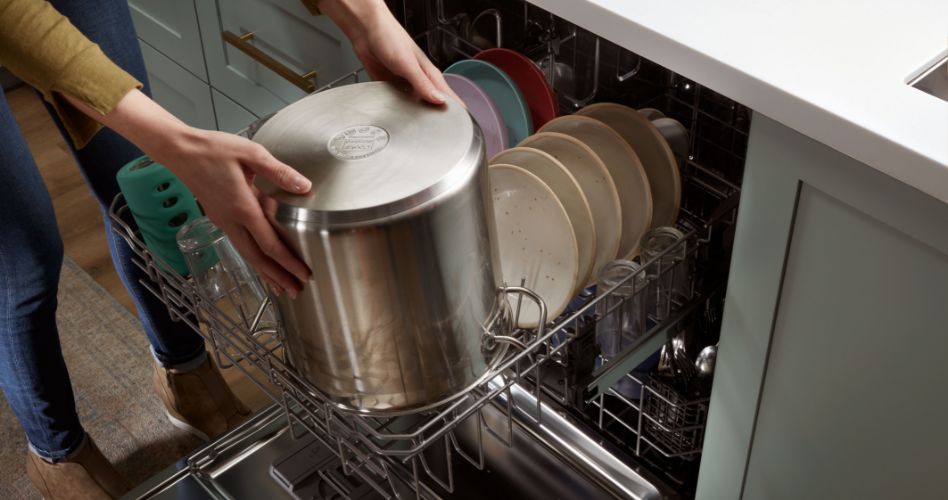 Someone loading a tall pot on the upper rack of a Whirlpool Dishwasher. 