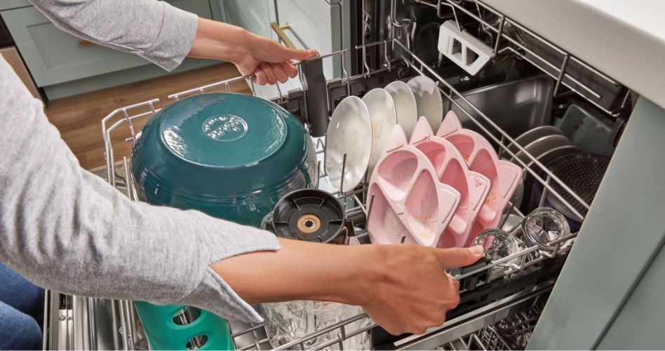 Someone pulling out the middle rack of a Whirlpool Dishwasher. The rack is full of kids' plates, bowls, plates and more.