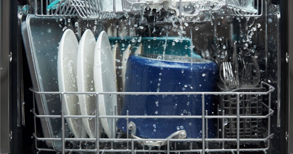The inside of a Whirlpool Dishwasher that's mid-wash cycle. On the rack are a baking tray, plates, pots, and cutlery in a cutlery tray.