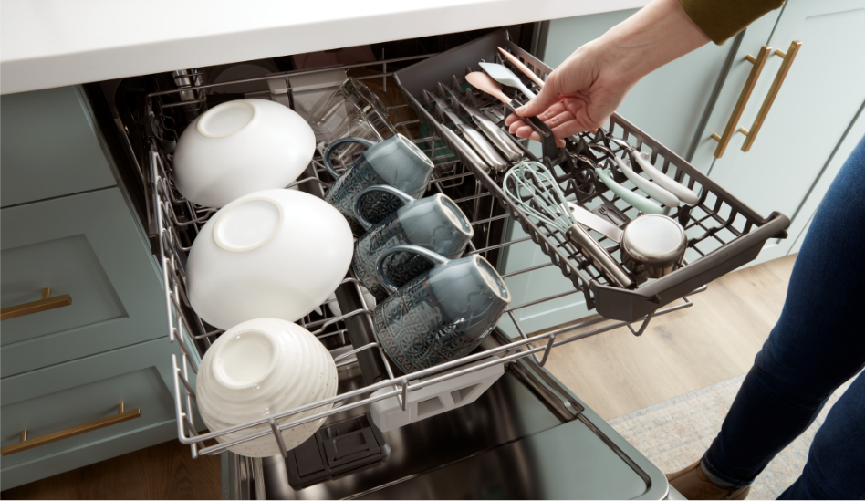 A woman placing utensils into the third rack of a dishwasher.