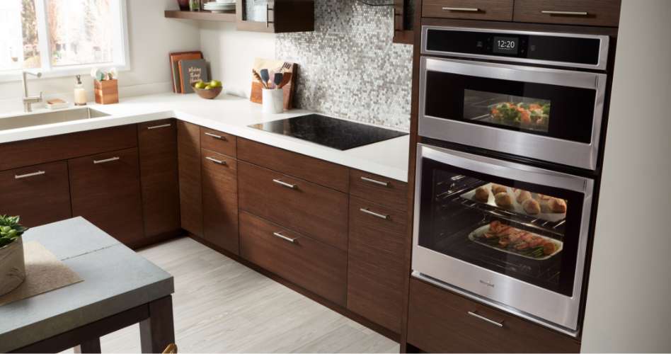 Whirlpool Combination Microwave Un four mural combiné Whirlpool en acier inoxydable encastré dans une armoire de cuisine avec des comptoirs en bois. De la nourriture cuit dans le four