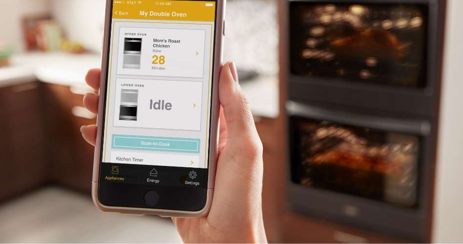 Whirlpool Combination Microwave Une personne est devant un four mural double et tient un téléphone intelligent avec un écran qui affiche les fonctions intelligentes d'un four mural Whirlpool