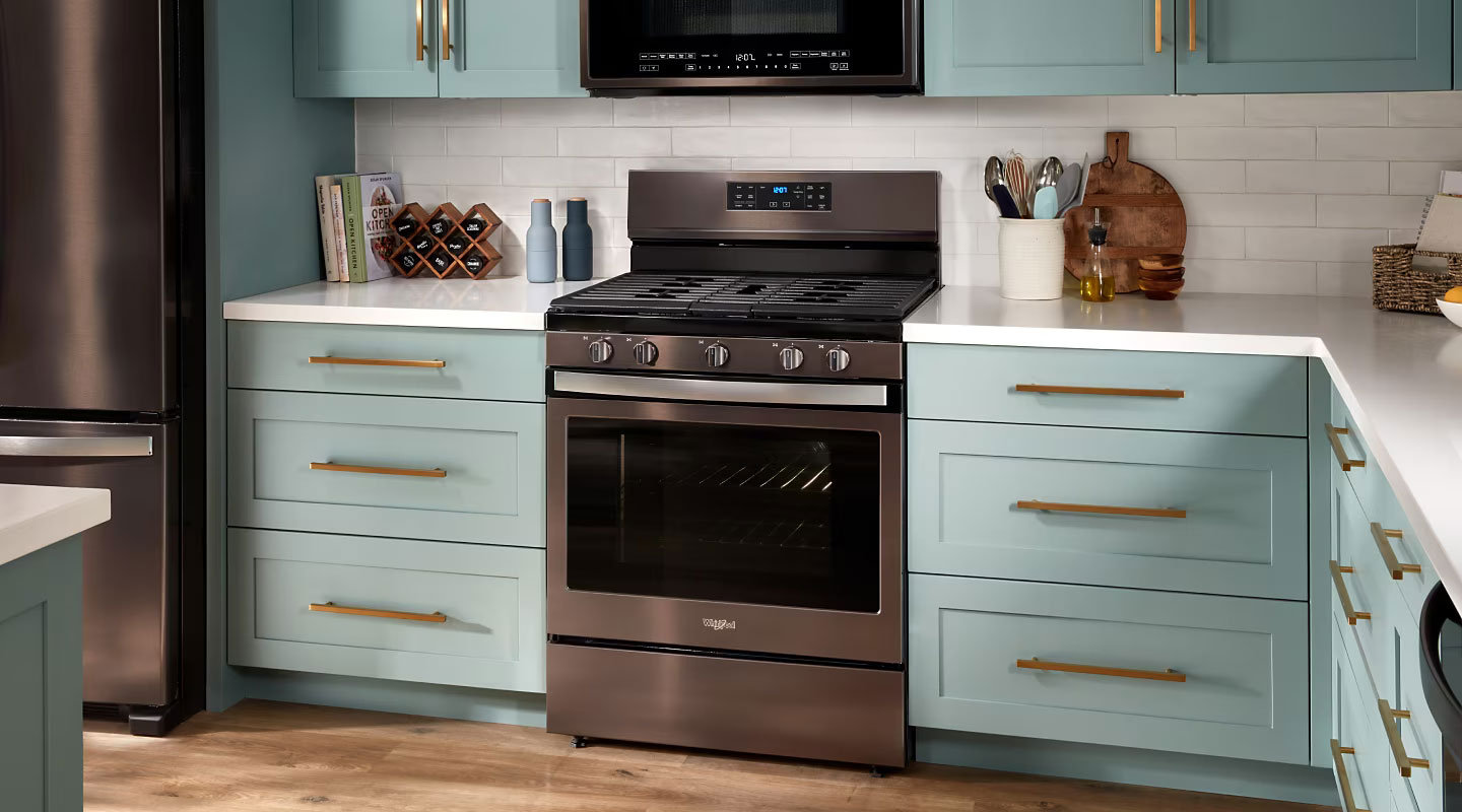 Whirlpool Combination Microwave Une cuisine équipée d'une cuisinière Whirlpool et d'un four à micro-ondes. Sur les comptoirs se trouvent des livres de cuisine, un porte-épices avec des épices, deux récipients, un porte-ustensiles de cuisine, une planche à découper, un récipient rempli d'huile, un panier avec des cahiers et un bol avec des citrons