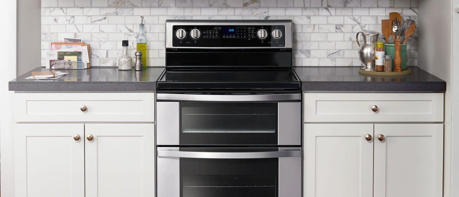 Whirlpool Combination Microwave Une cuisine avec un four double Whirlpool. À gauche du four se trouvent une bouteille d'huile, une salière et une poivrière, un porte-lettres avec du courrier et un carnet de notes sur lequel sont posés des papiers. À droite du four se trouvent un porte-ustensiles de cuisine, un pichet et des récipients d'assaisonnement sur un plateau circulaire vert