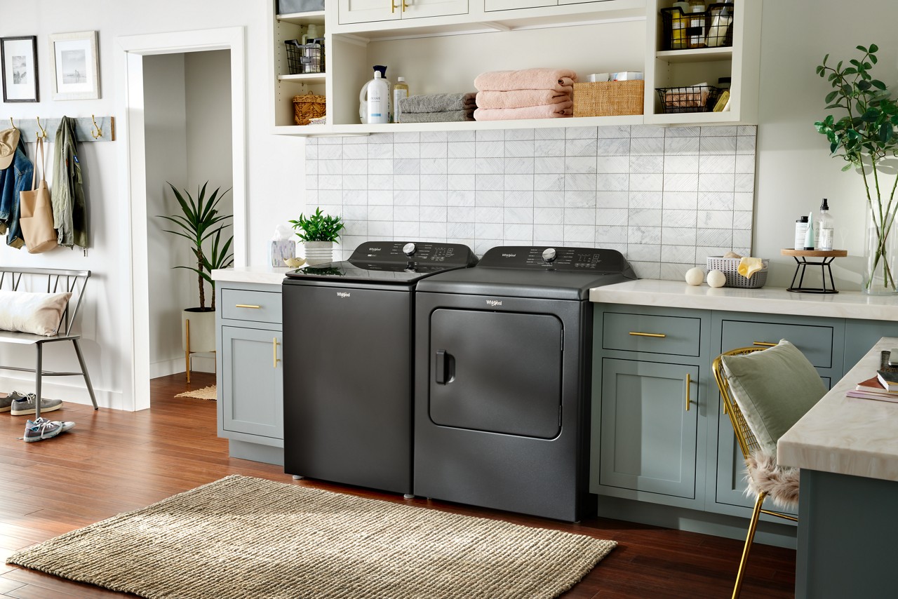 Un ensemble laveuse-sécheuse Whirlpool® dans une grande salle de lavage. Des serviettes pliées et divers articles de lessive sont disposés sur les étagères au-dessus.