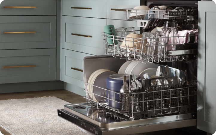 Un lave-vaisselle se trouve dans une cuisine avec des armoires grises. Il est ouvert et les paniers sont sortis. Chaque grille est pleine de divers articles, tels que des assiettes, des bols, des tasses et plus
