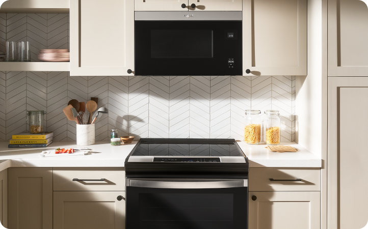 Une cuisine avec une cuisinière et un four à micro-ondes à hotte intégrée Whirlpool. Sur les comptoirs se trouvent un porte-ustensiles, des contenants de pâtes, des livres de recettes et divers objets