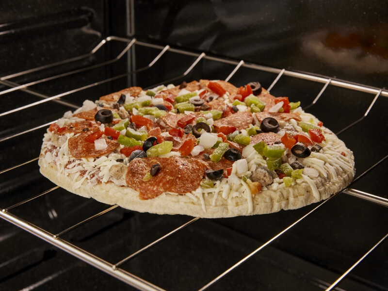 A frozen pizza with vegetables on top cooking in an oven A frozen pizza with vegetables on top cooking in an oven