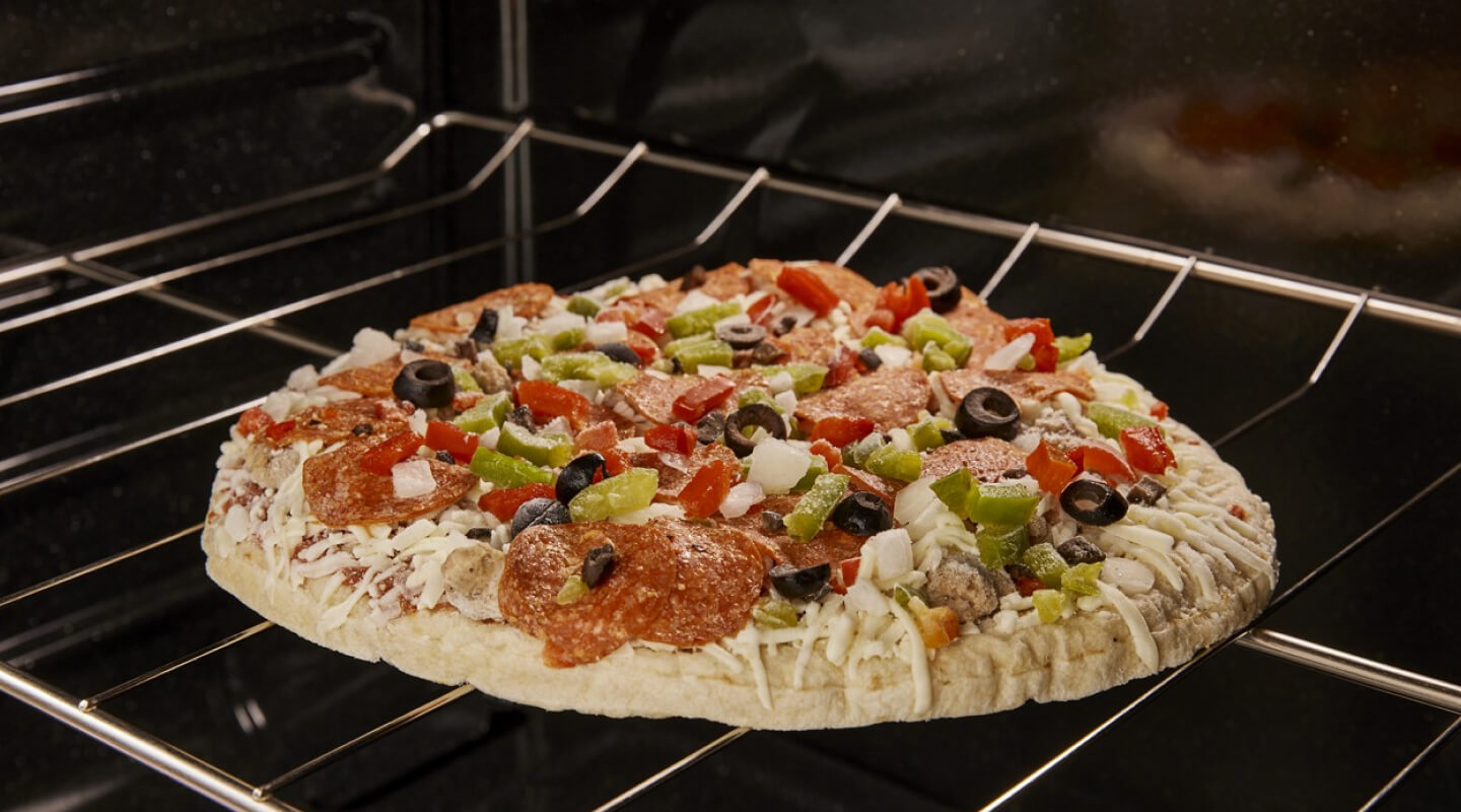 A frozen pizza with vegetables on top cooking in an oven A frozen pizza with vegetables on top cooking in an oven