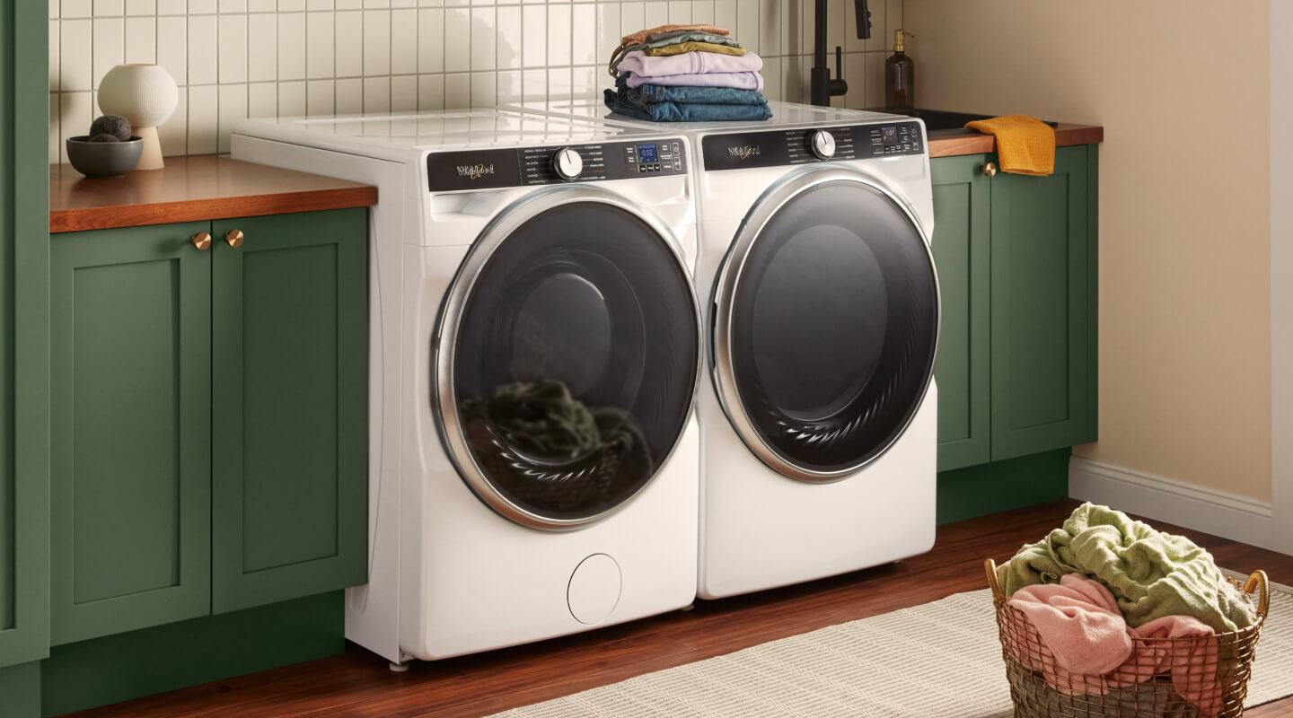 Une laveuse et une sécheuse Whirlpool® blanches à chargement frontal à côté d’armoires vertes