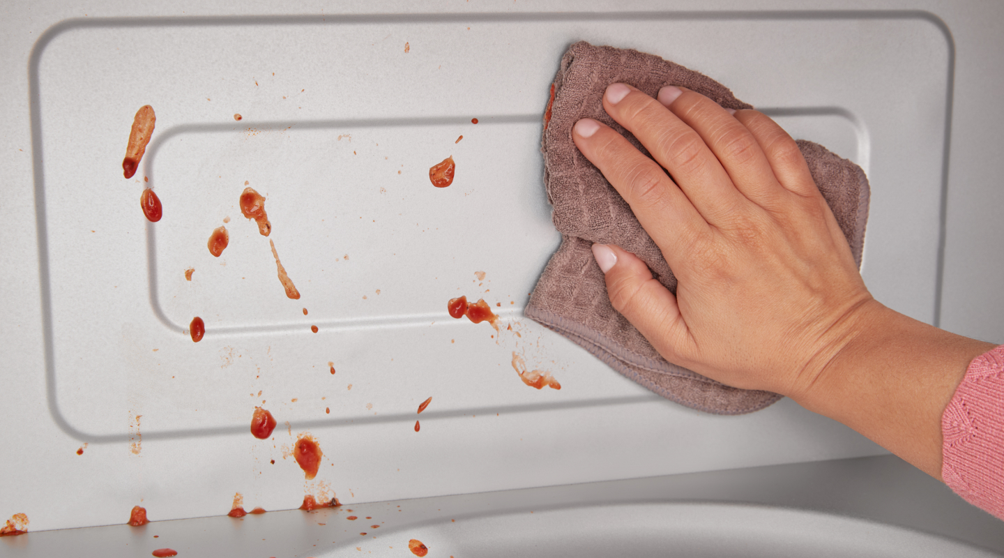 Person wiping splatters from microwave interior with rag Person wiping splatters from microwave interior with rag