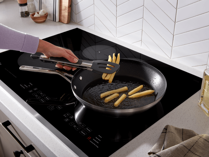 Person frying french fries in a frying pan on top of an induction cooktop Person frying french fries in a frying pan on top of an induction cooktop