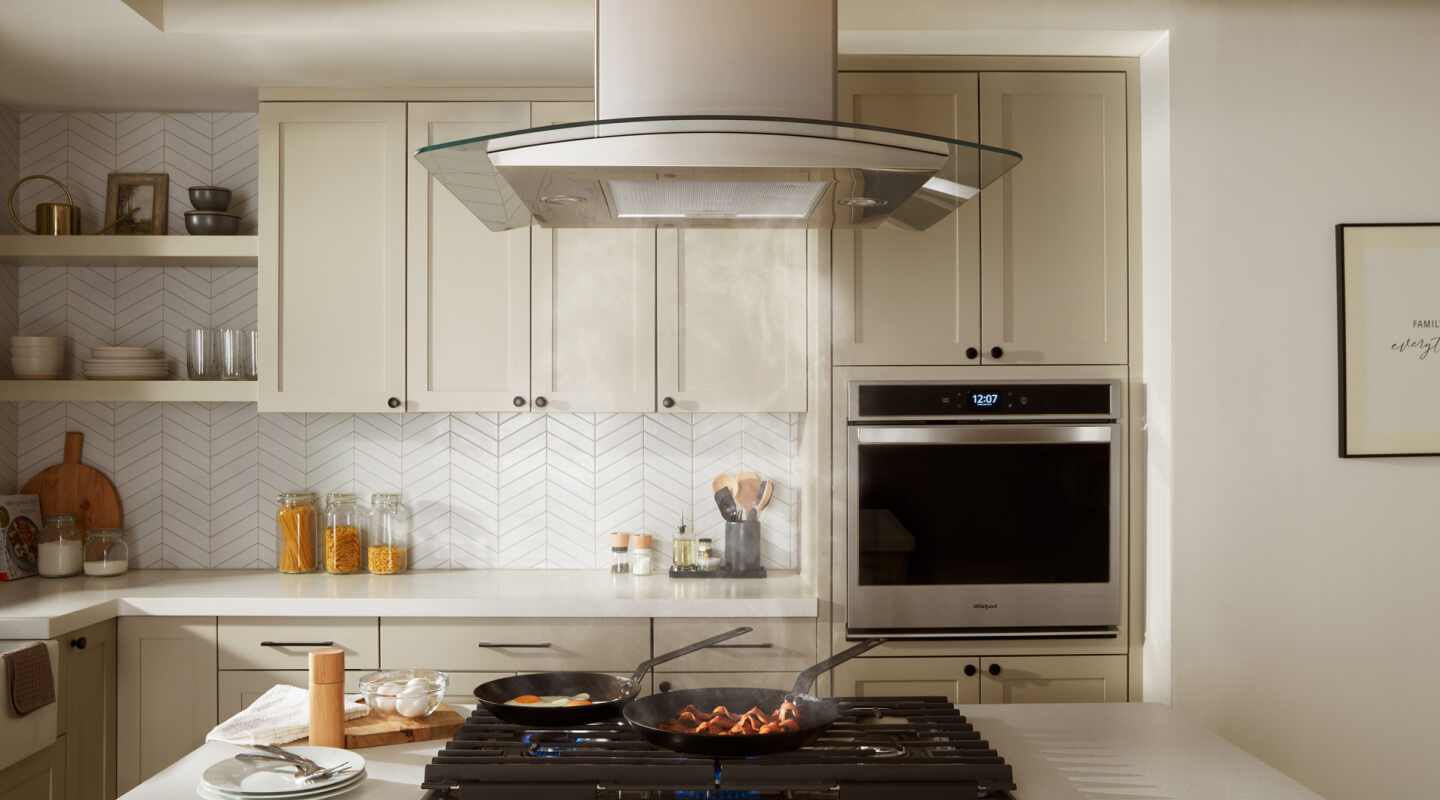 Bacon and eggs simmering on a gas cooktop underneath an island canopy hood