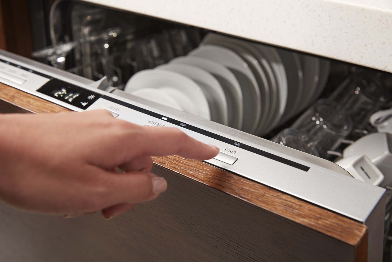 A hand selecting a control on a Whirlpool® Top Control Dishwasher