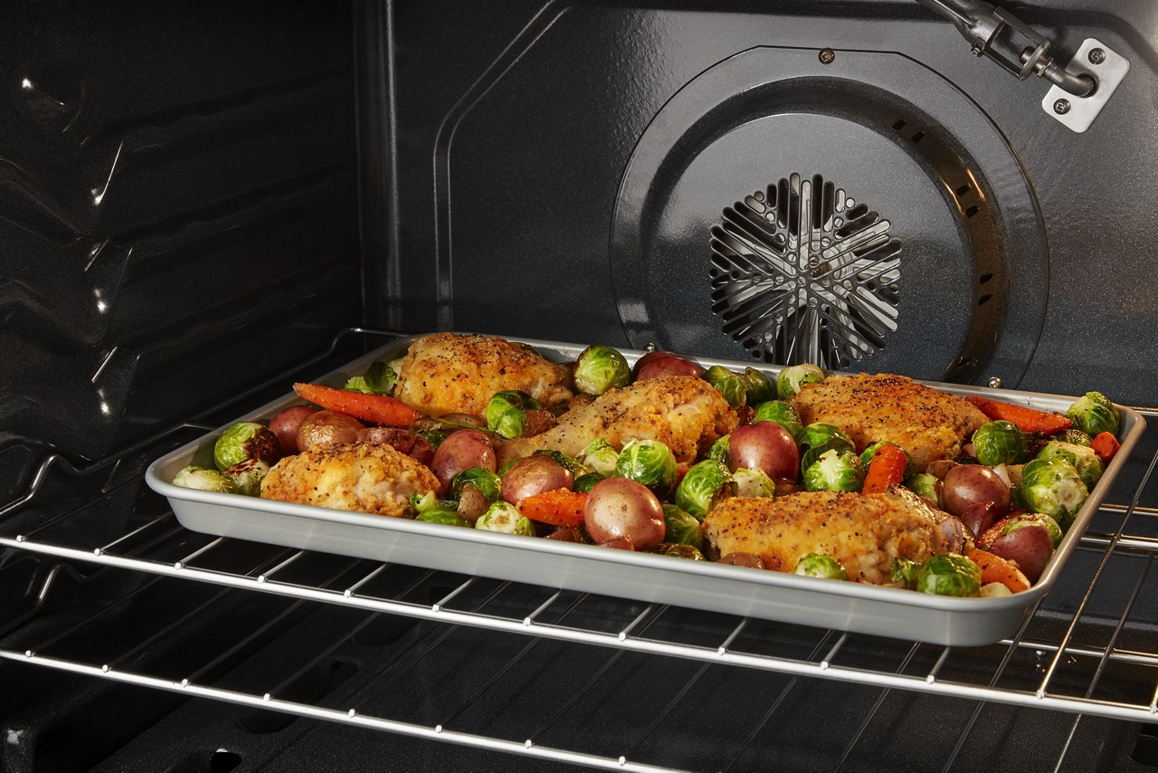 A tray of roasted chicken and vegetables inside an oven.