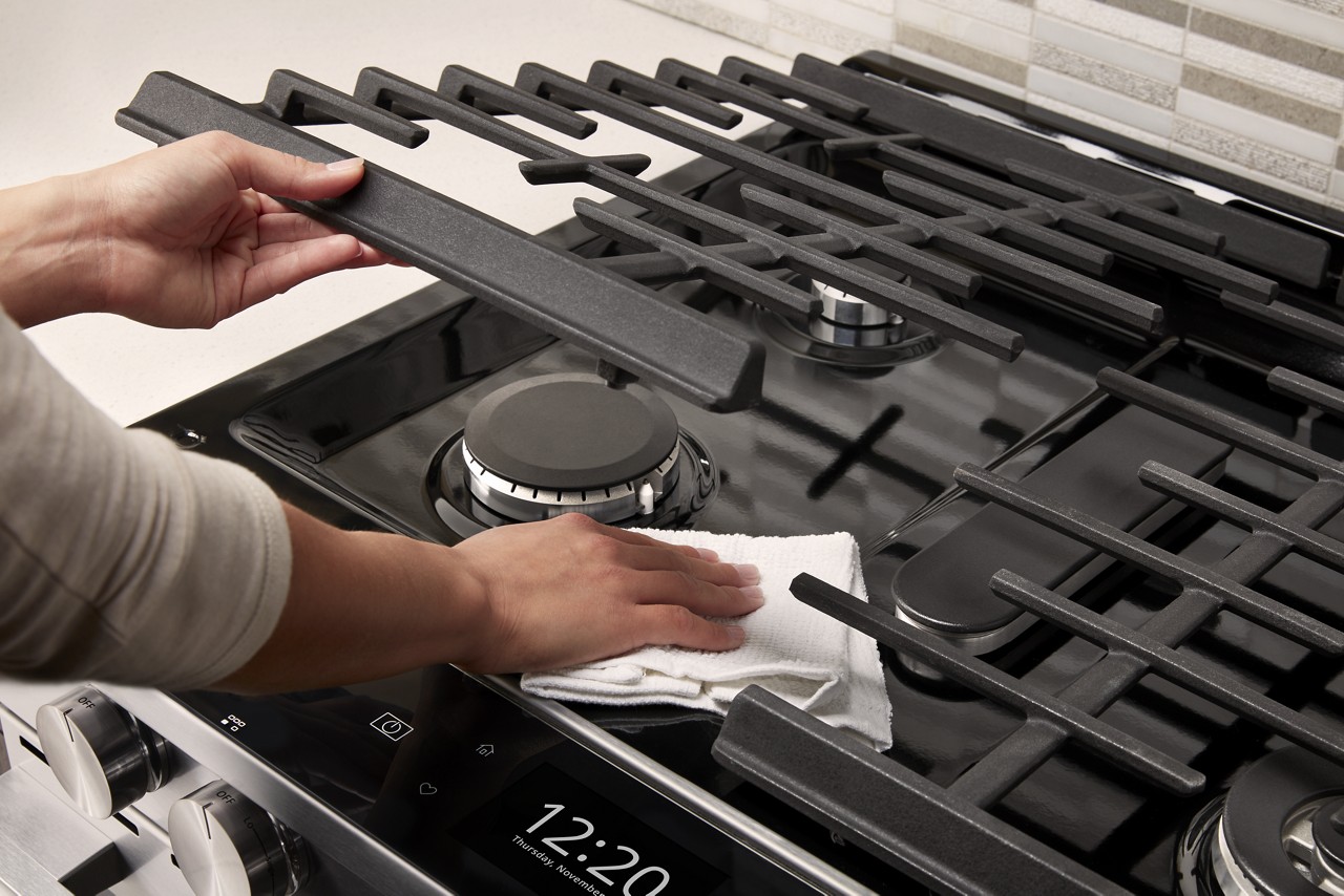 A person lifts up metal cooking grates to wipe the surface underneath.