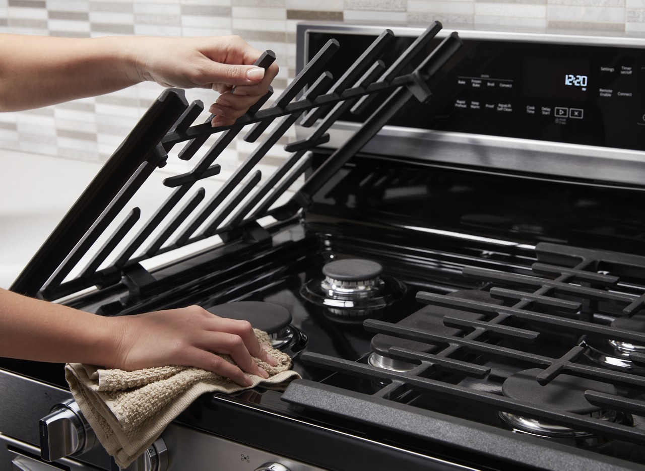 A person lifts up cooking grates to wipe the front of a stove.