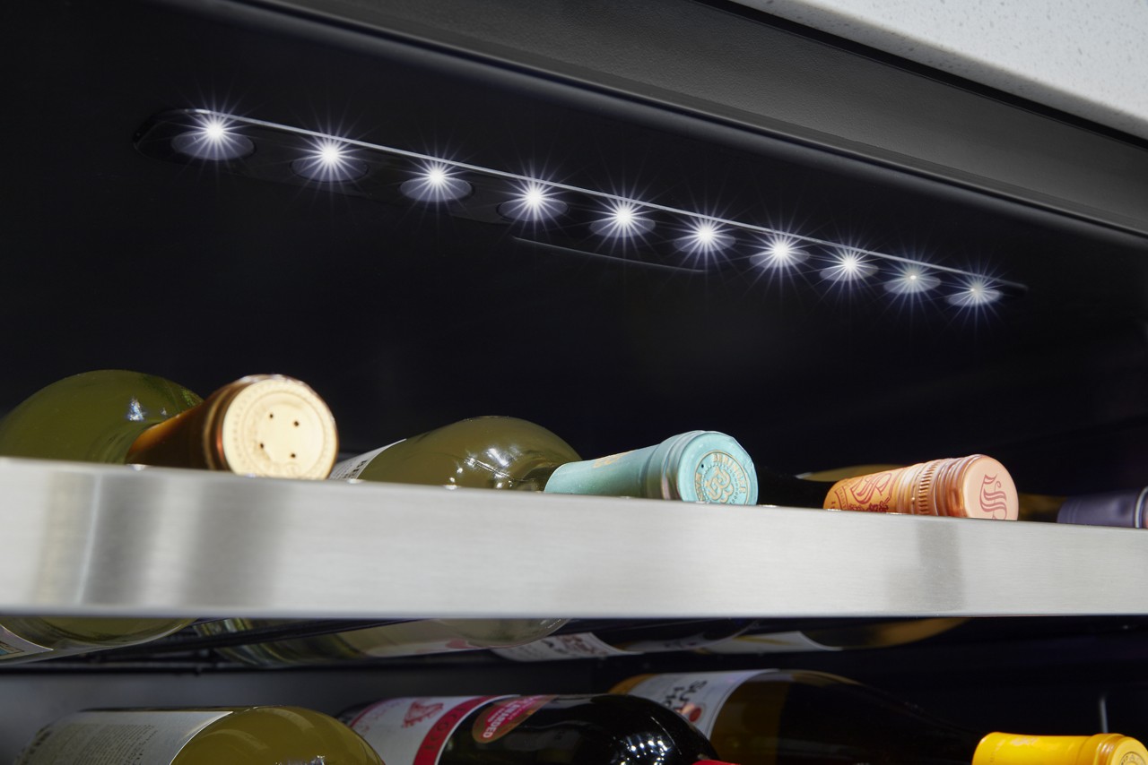 A close-up of wine bottles on shelves in a wine refrigerator.