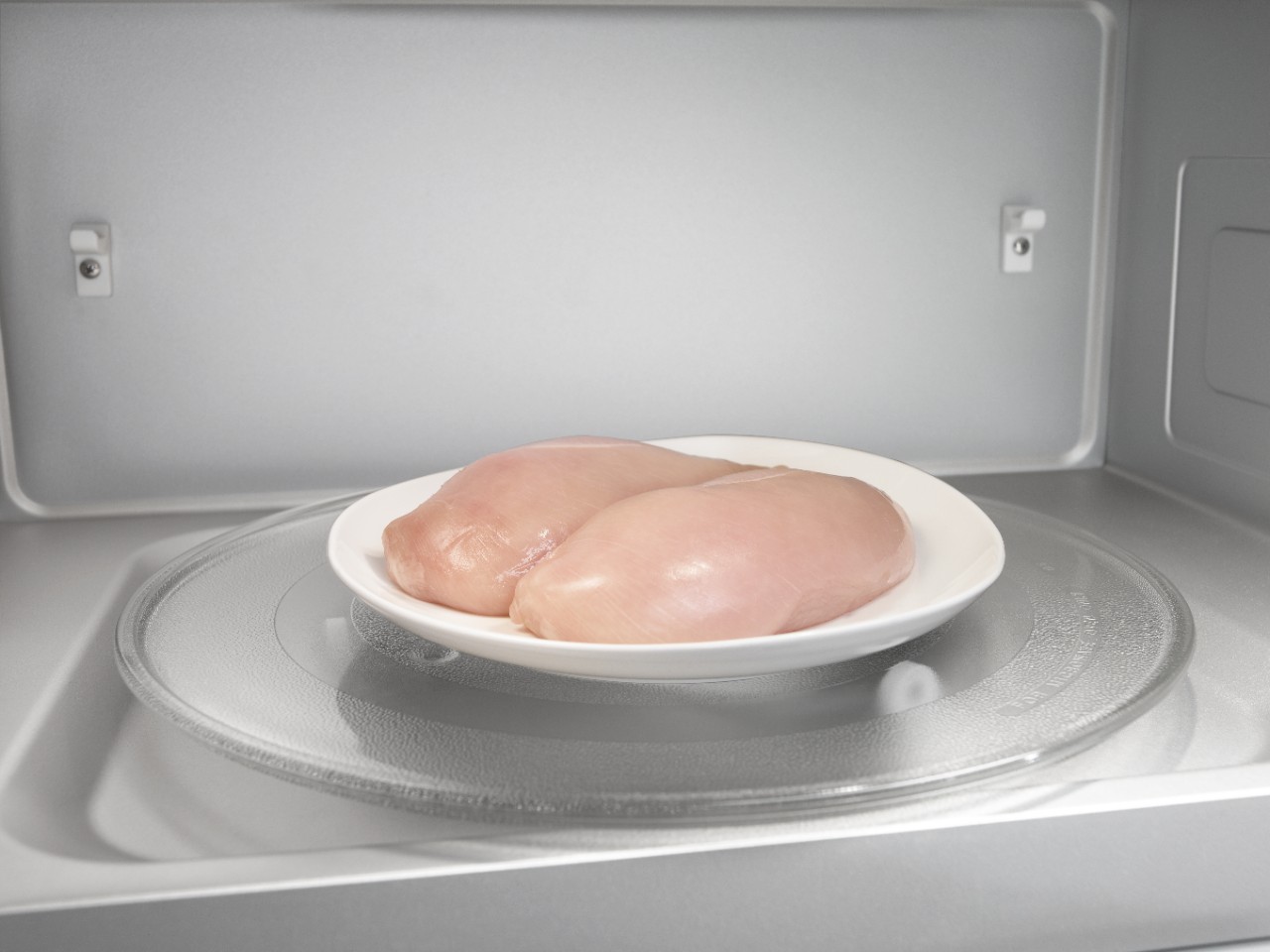 Two chicken breasts on a plate in a microwave.