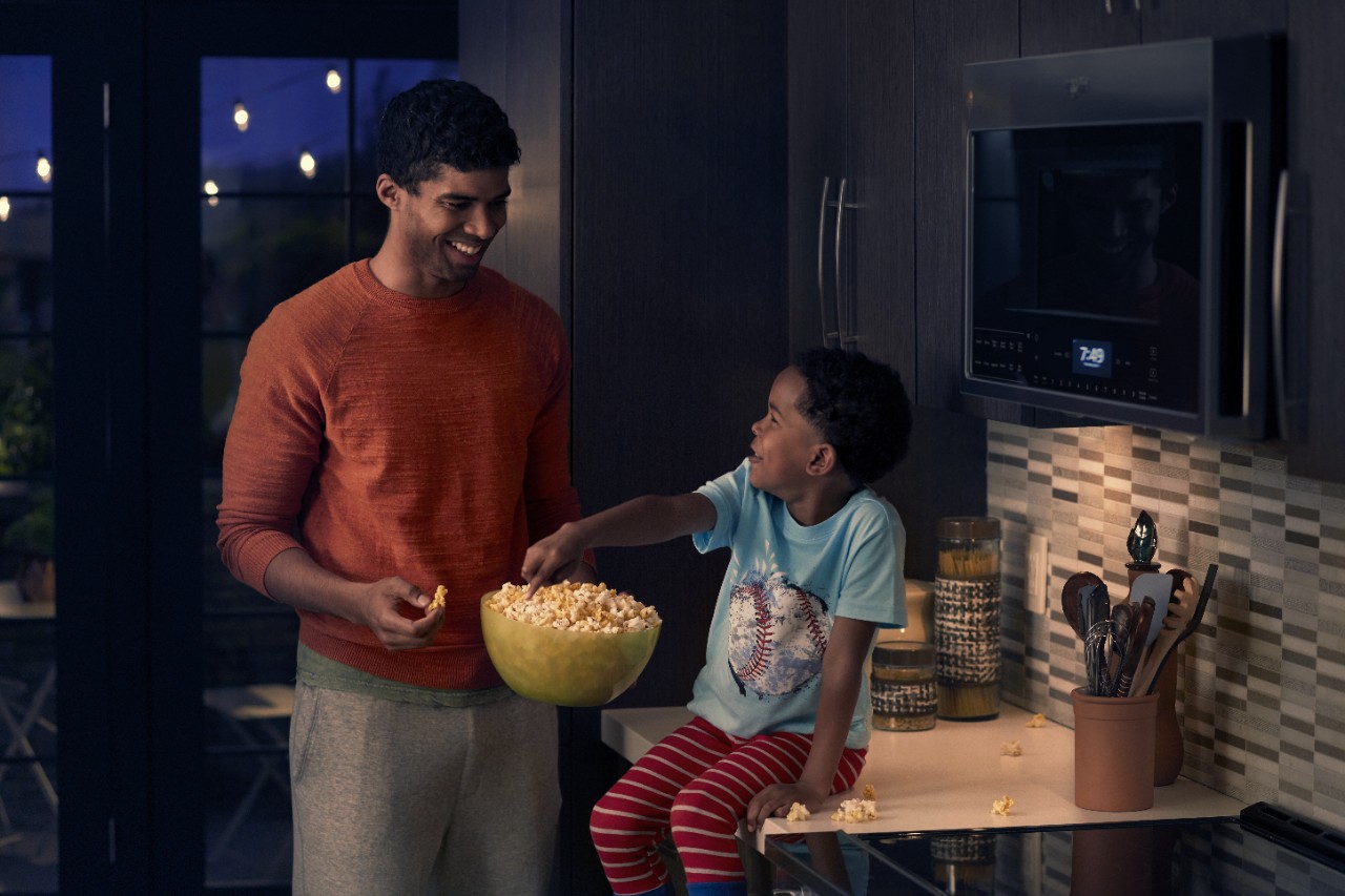 A father and his child share popcorn in a kitchen at night. A father and his child share popcorn in a kitchen at night.
