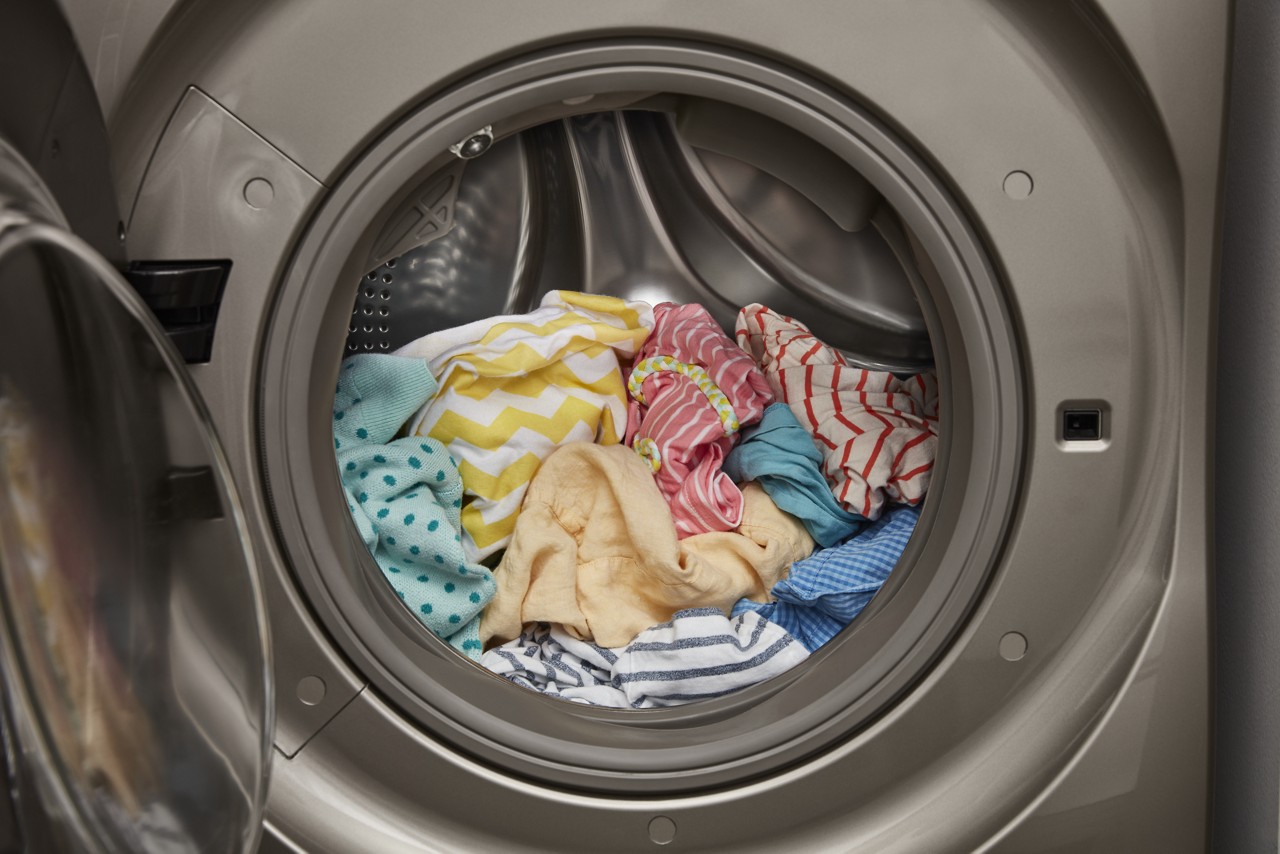 Pastel clothes loaded into a washer or dryer with an open door. Pastel clothes loaded into a washer or dryer with an open door.