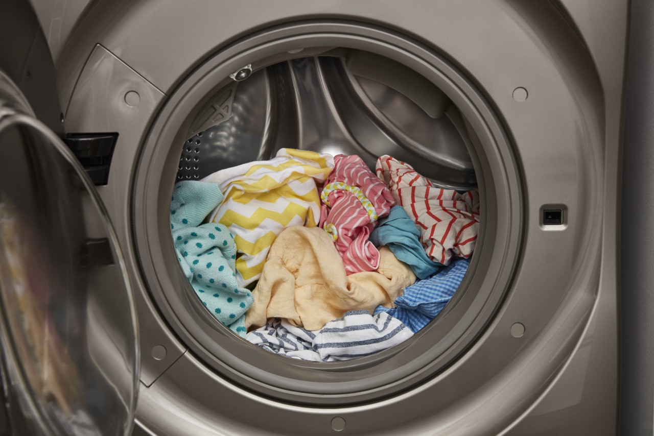 Pastel clothes loaded into a washer or dryer with an open door.