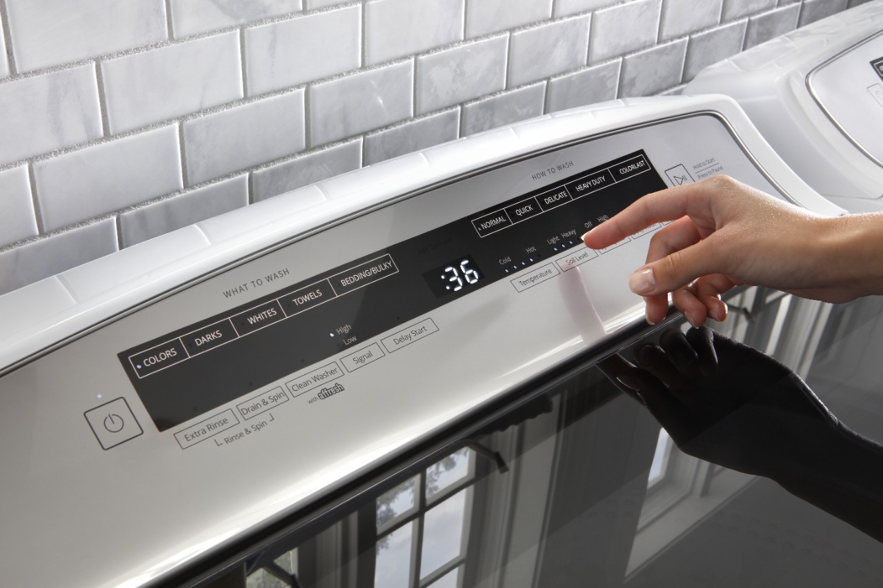A person uses a washer or dryer control panel to choose a cycle. A person uses a washer or dryer control panel to choose a cycle.