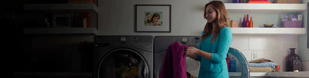 A person getting clothing out of a washer or dryer.