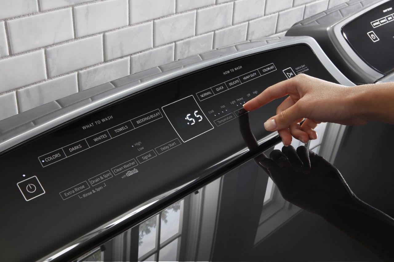 A person uses a washer or dryer control panel to choose a laundry cycle. A person uses a washer or dryer control panel to choose a laundry cycle.