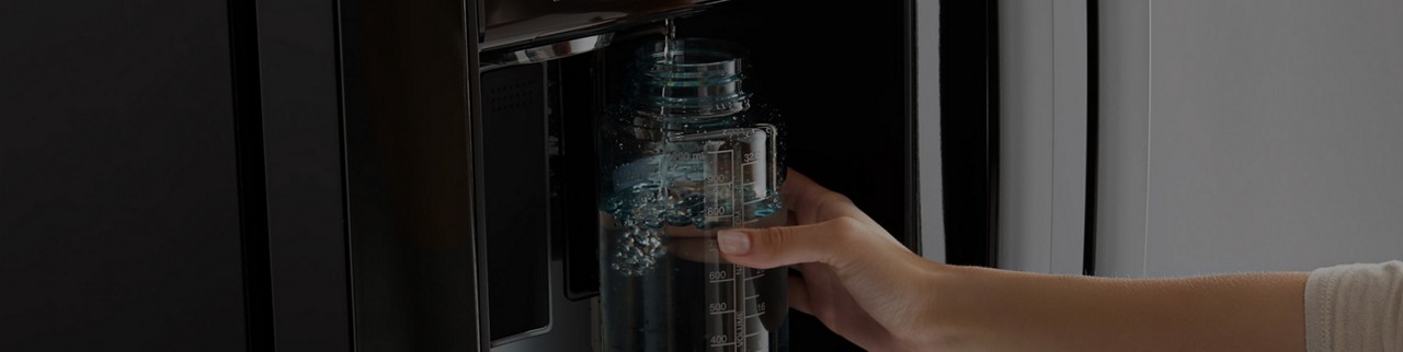 A woman fills up a water bottle from a refrigerator water dispenser.