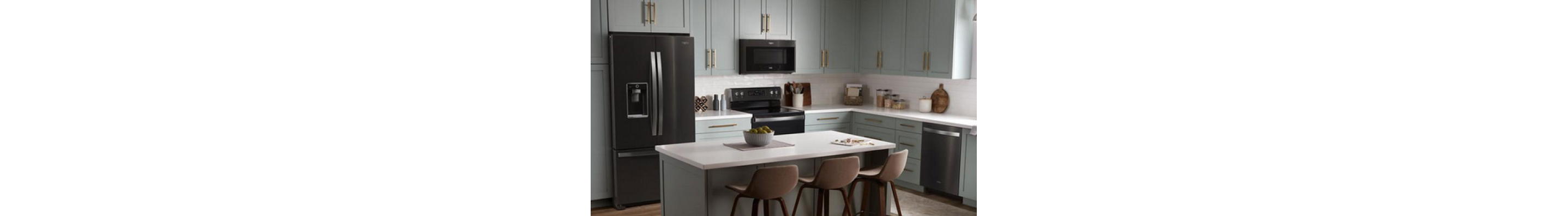 A kitchen with an island and three stools. On the island is a bowl of fruit on a placemat. The cupboards are grey and the Whirlpool Black Stainless Steel Appliances include a refrigerator, an oven with an over-the-range microwave and a dishwasher. On the counters are a kitchen utensil holder, cutting boards, a potted plant, salt and pepper shakers and more