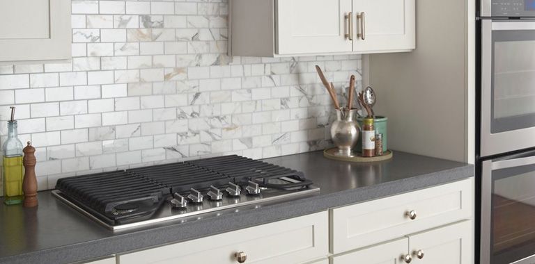 Whirlpool Gas Cooktop in Modern Kitchen with White Cupboards and Grey Stone Backsplash